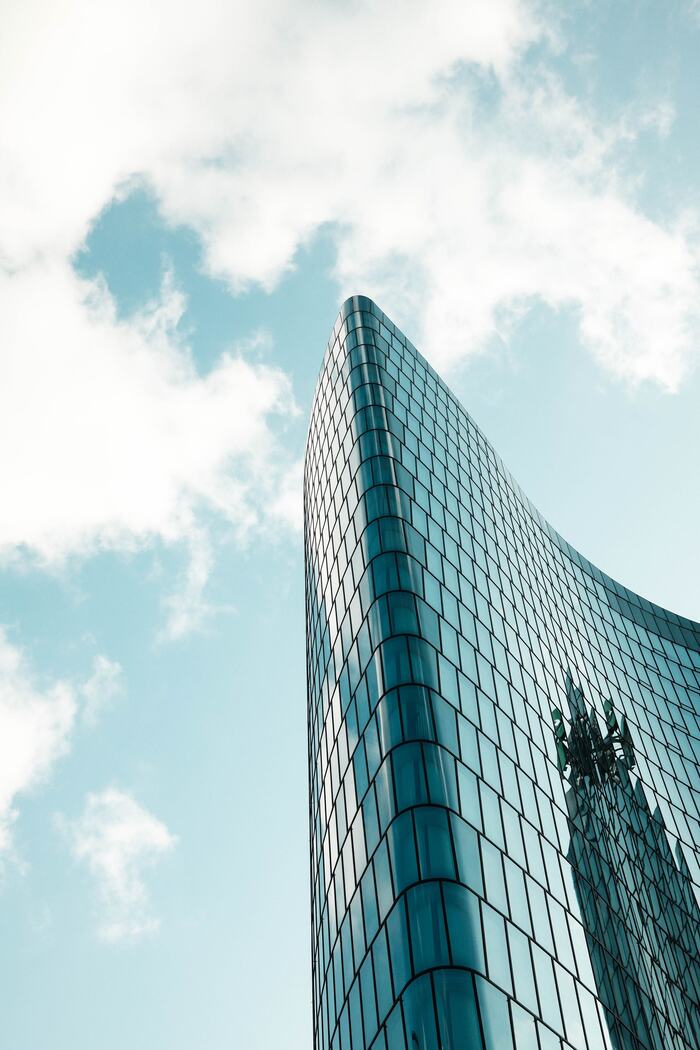 Modernes, geschwungenes Glashochhaus vor blauem Himmel